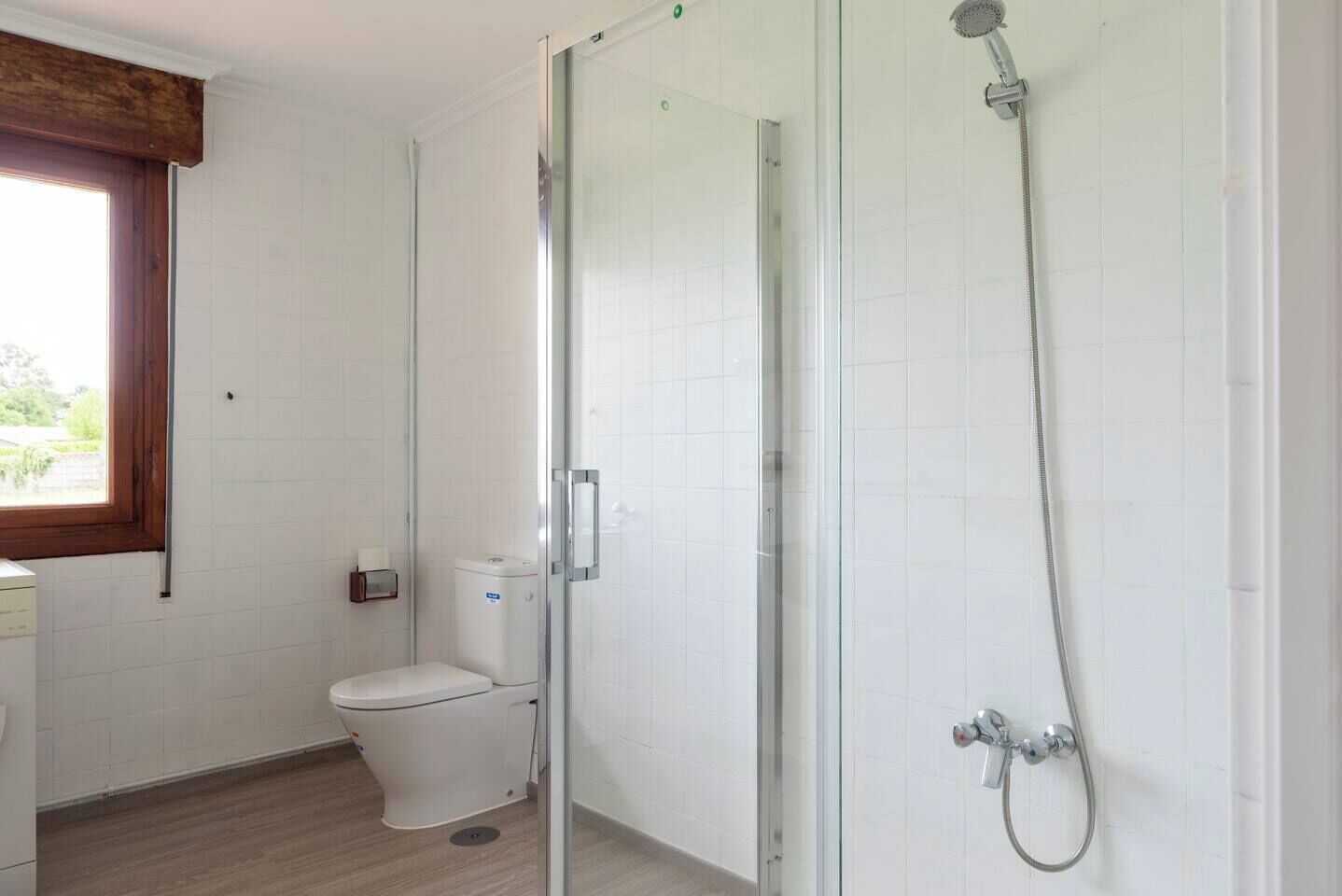 A bathroom with a glass shower enclosure, a toilet, and a window with a wooden frame.