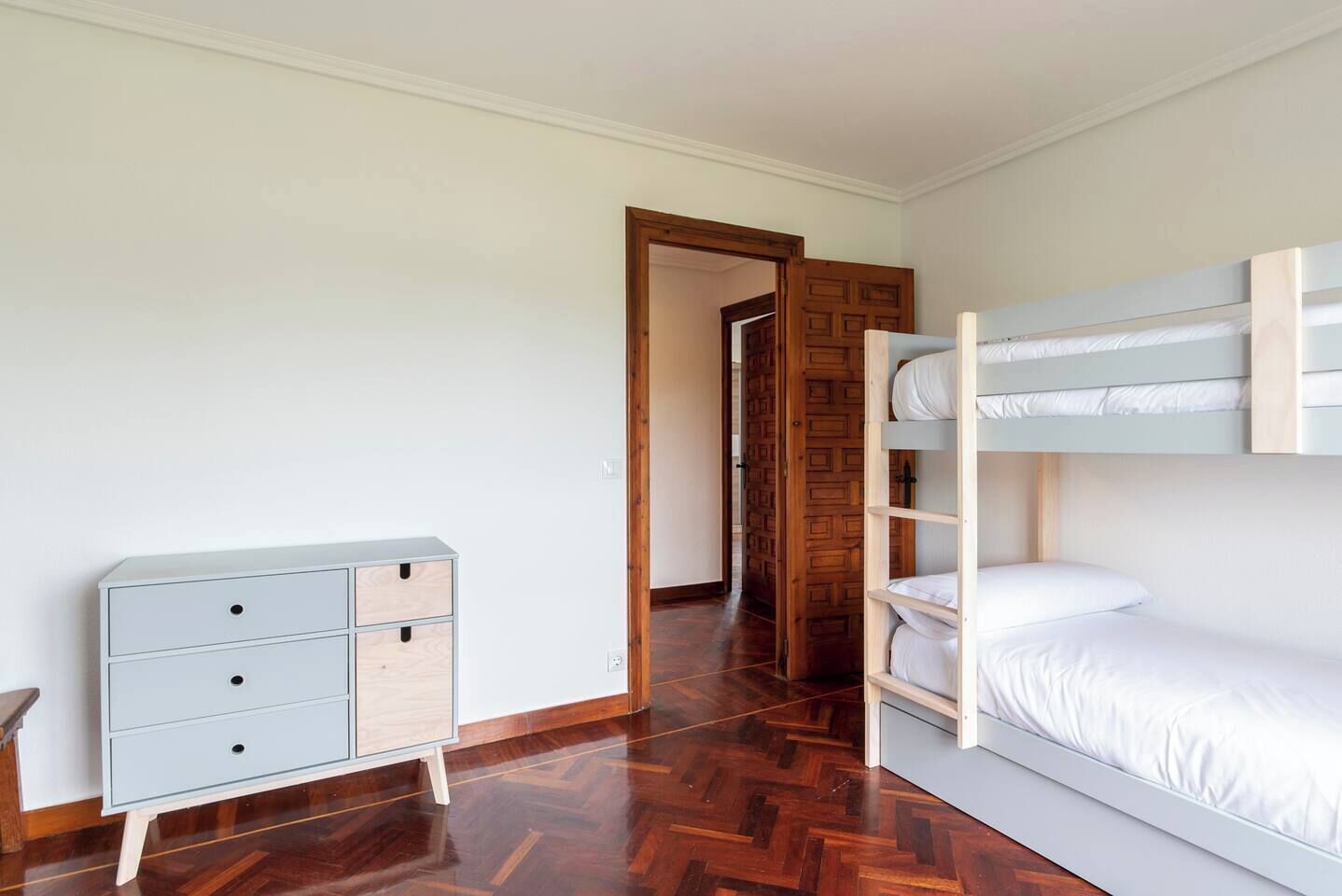 A room with a bunk bed, a dresser with drawers, and a wooden door.