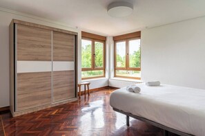 A bedroom with a bed, wooden wardrobe, two windows, and a radiator.