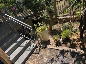 Eine Treppe mit Metallgeländern führt zu einem Gartenbereich mit Kübelpflanzen und einem Baum.