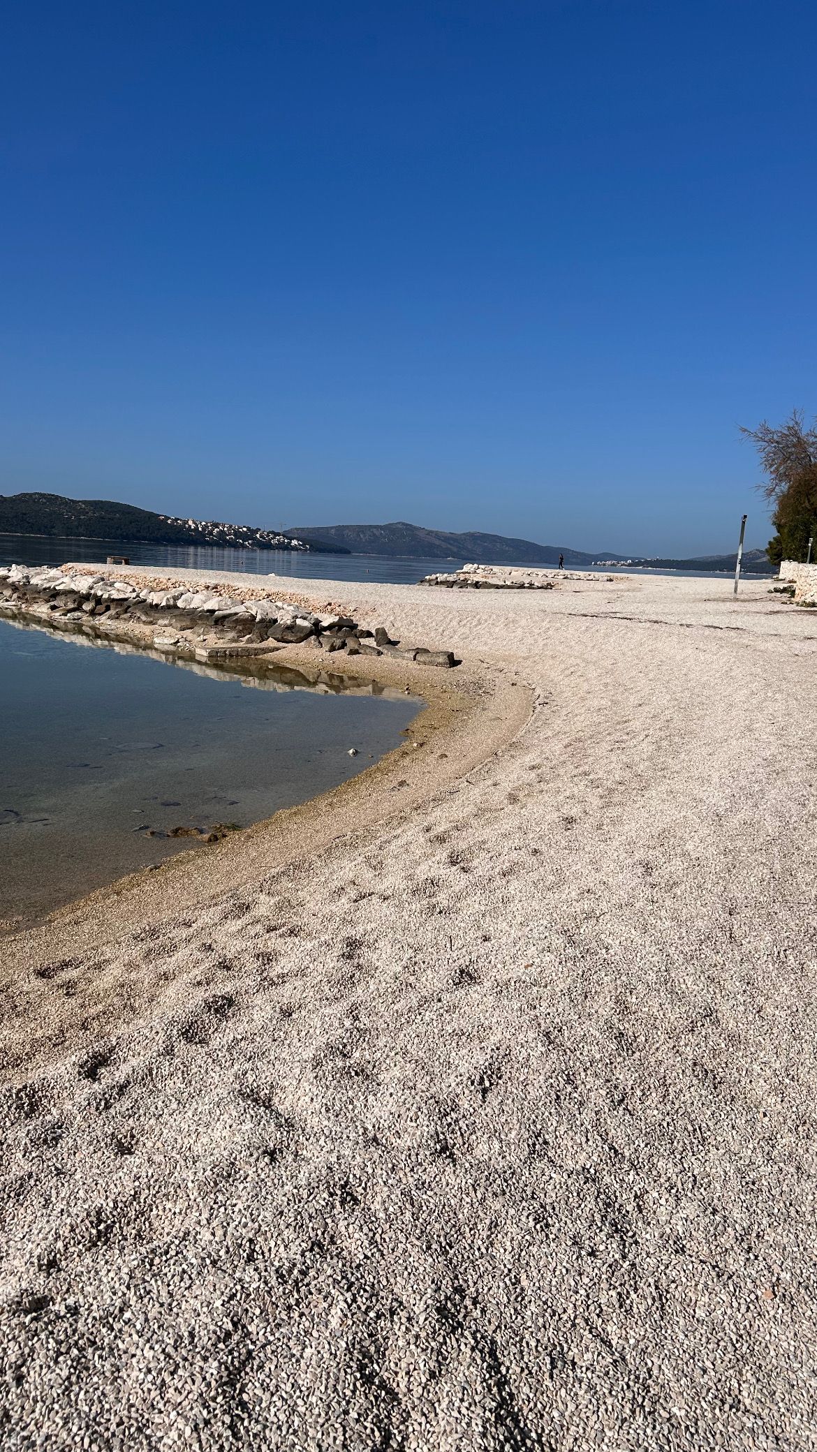 A pebbled beach with a clear sky and distant hills.