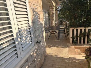 A patio area with a stone wall, a table with chairs, and a white fence. - Apartment Mediteran Okrug Gornji (Okrug Gornji)