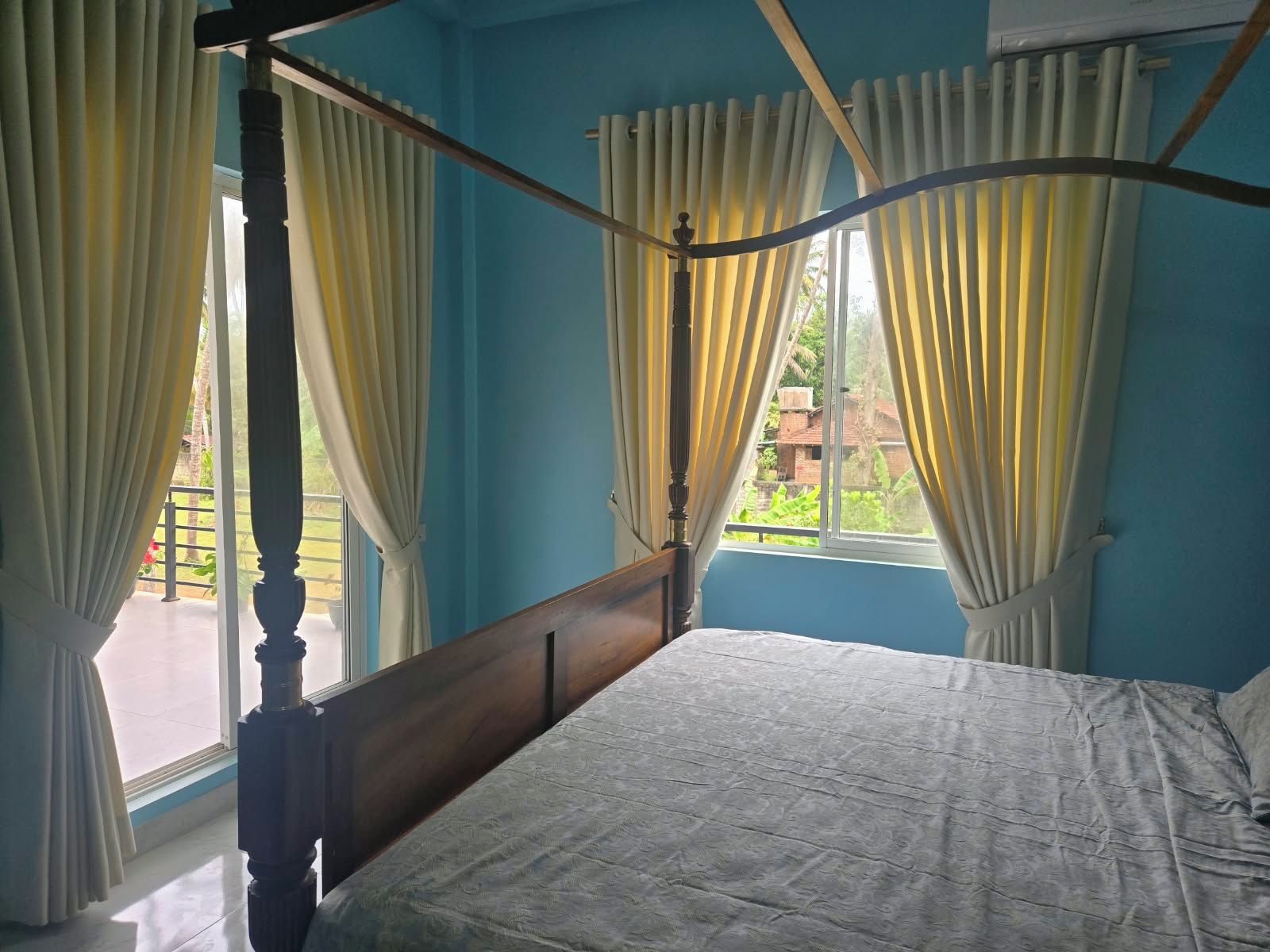 A four-poster bed with a wooden headboard in a room with blue walls and white curtains.