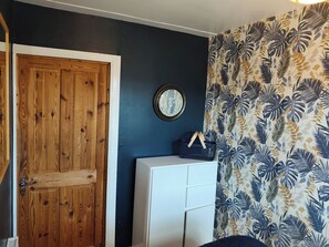 Ein Zimmer mit einer Holztür, einem weißen Schrank und einer Wand mit tropischem Blattmuster.