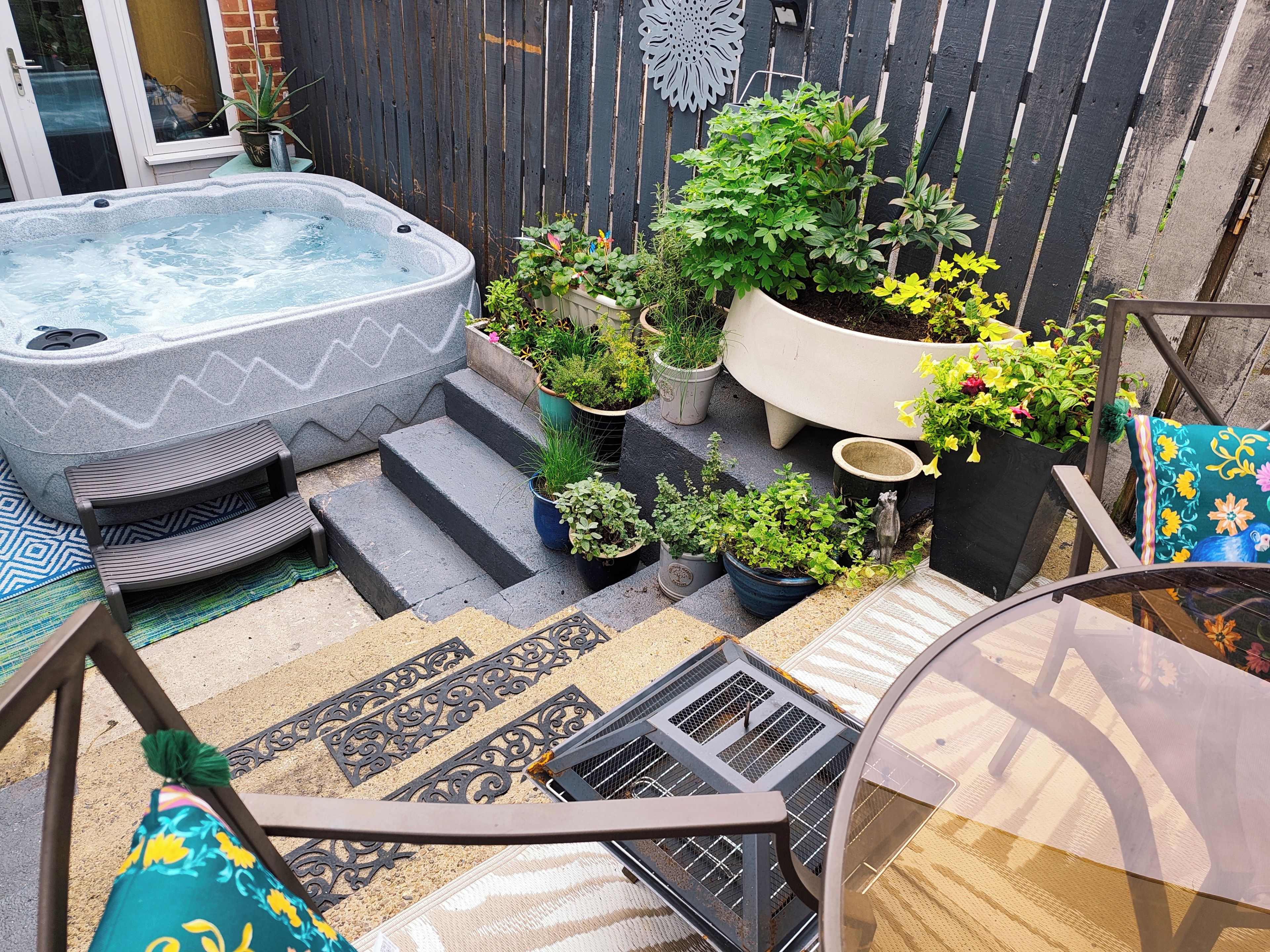 A hot tub, outdoor seating, steps, and potted plants in a backyard setting.