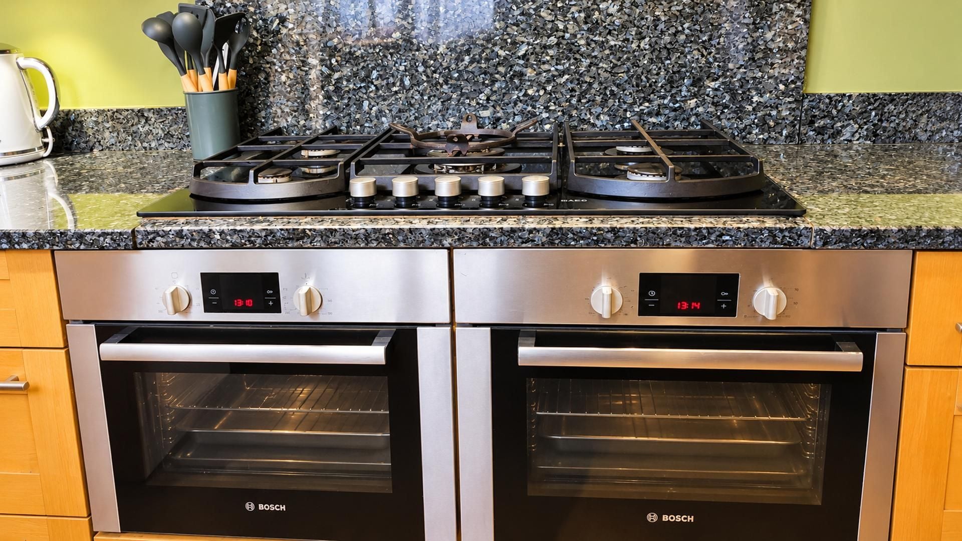 A kitchen with a gas stove, two ovens, and a granite countertop.