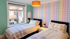 Une chambre avec deux lits, une fenêtre donnant sur un beau paysage et un mur décoré d’un motif coloré en forme de cœur.