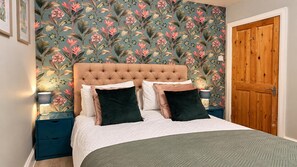 Quarto com cabeceira estofada, cama com várias almofadas, mesa de cabeceira com abajur e porta de madeira.