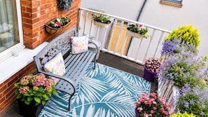 Un balcon avec un banc, des plantes en pot et une rambarde.