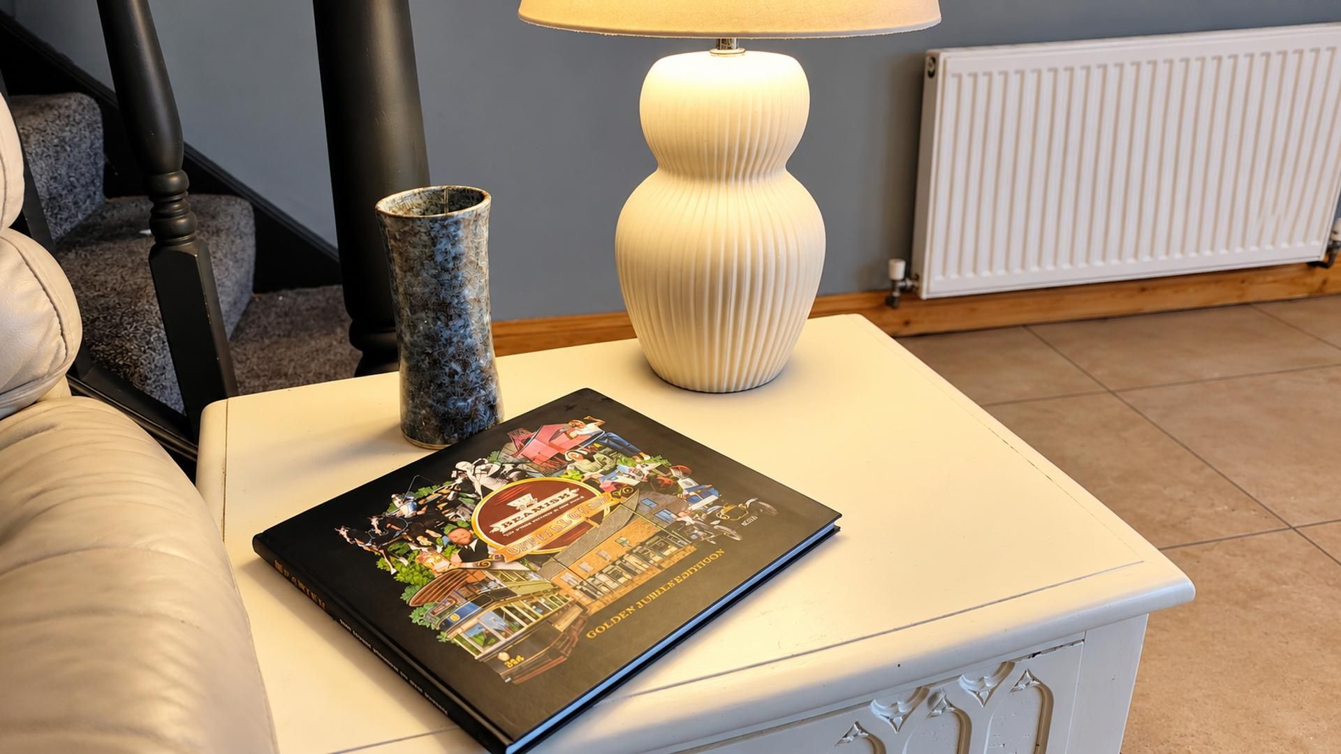 A book titled 'Golden Jubilee Edition' on a white table with a lamp and a vase.