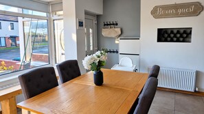 A dining area with a wooden table and four chairs, a vase with flowers, a coat rack, a sign that reads 'Be our guest,' and a radiator. - Hideaway House, Sleeps 6 With Hot Tub & Balcony (Chester-le-Street)