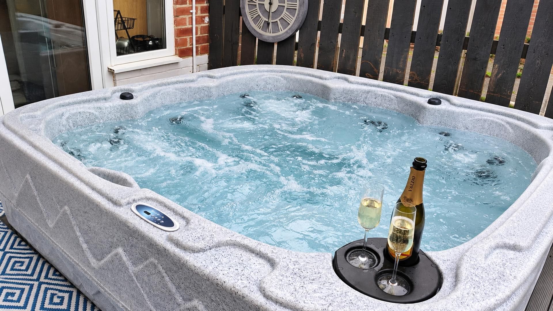 A hot tub with a control panel, two glasses of white wine, and a bottle of wine on a stand.