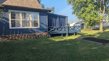 Een huis met een stenen fundering, een houten terras en een grote boom in de voortuin.