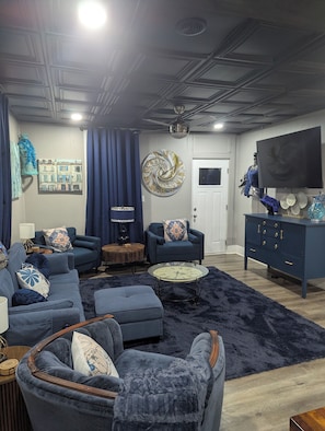 A modern living room with a dark blue sofa set, a round coffee table, and a large wall clock.