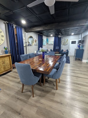 A dining area with a wooden table, blue upholstered chairs, a vase with flowers, and a ceiling fan.