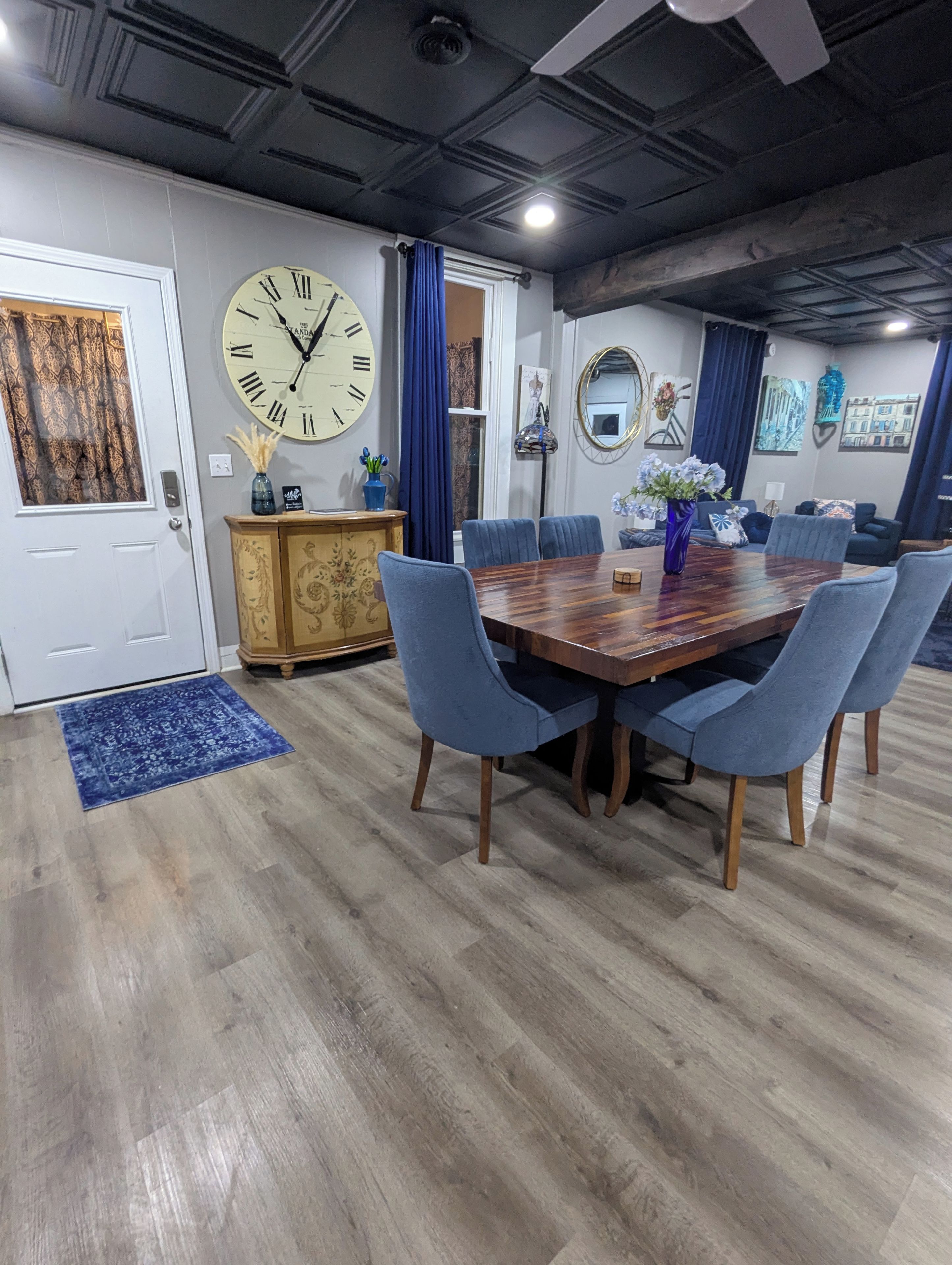 A dining area with a wooden table, blue chairs, a clock on the wall, and a blue rug.