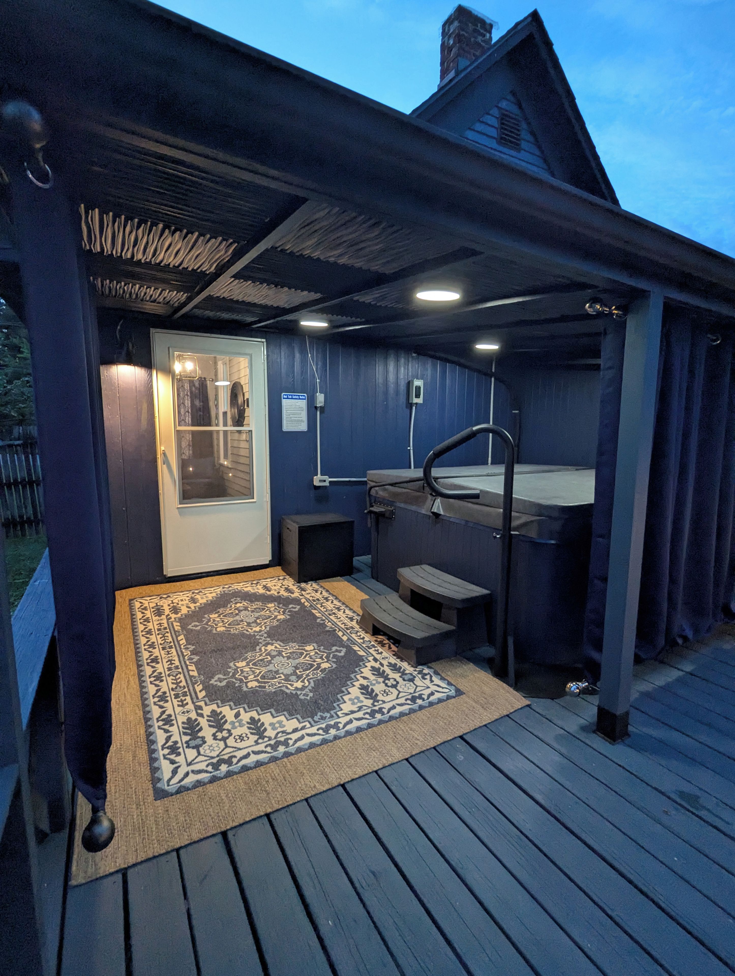 A covered outdoor area with a hot tub, a door, and a window.