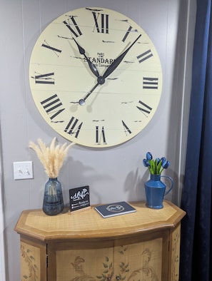 A wall-mounted clock with Roman numerals, a vase with pampas grass, a sign with a Wi-Fi password, and a blue vase with tulips.