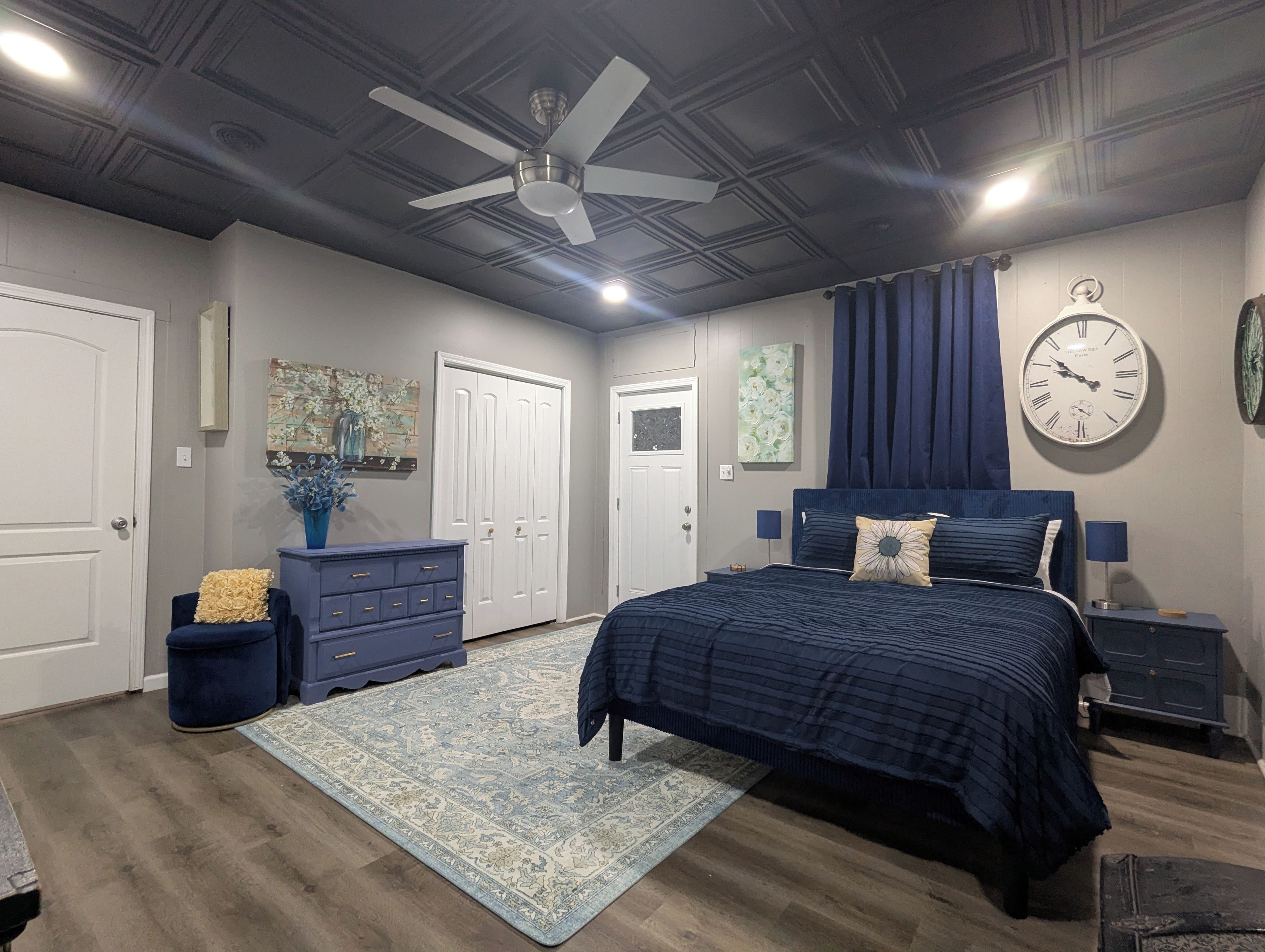 Une chambre à coucher comprenant un lit, une commode, des tables de chevet, une horloge et un ventilateur de plafond.