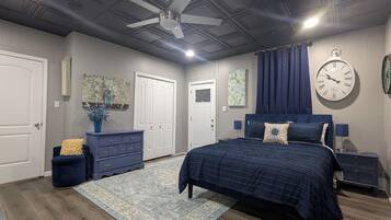 Une chambre à coucher comprenant un lit, une commode, des tables de chevet, une horloge et un ventilateur de plafond.
