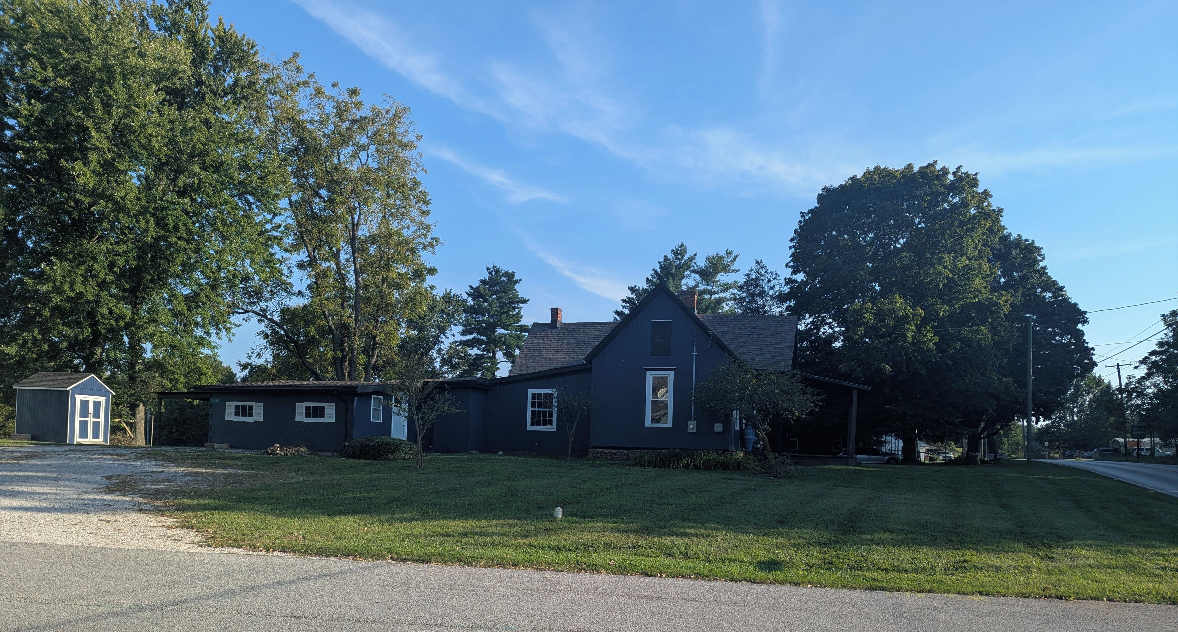 A residential house with a dark exterior, a sloped roof, and a front yard.