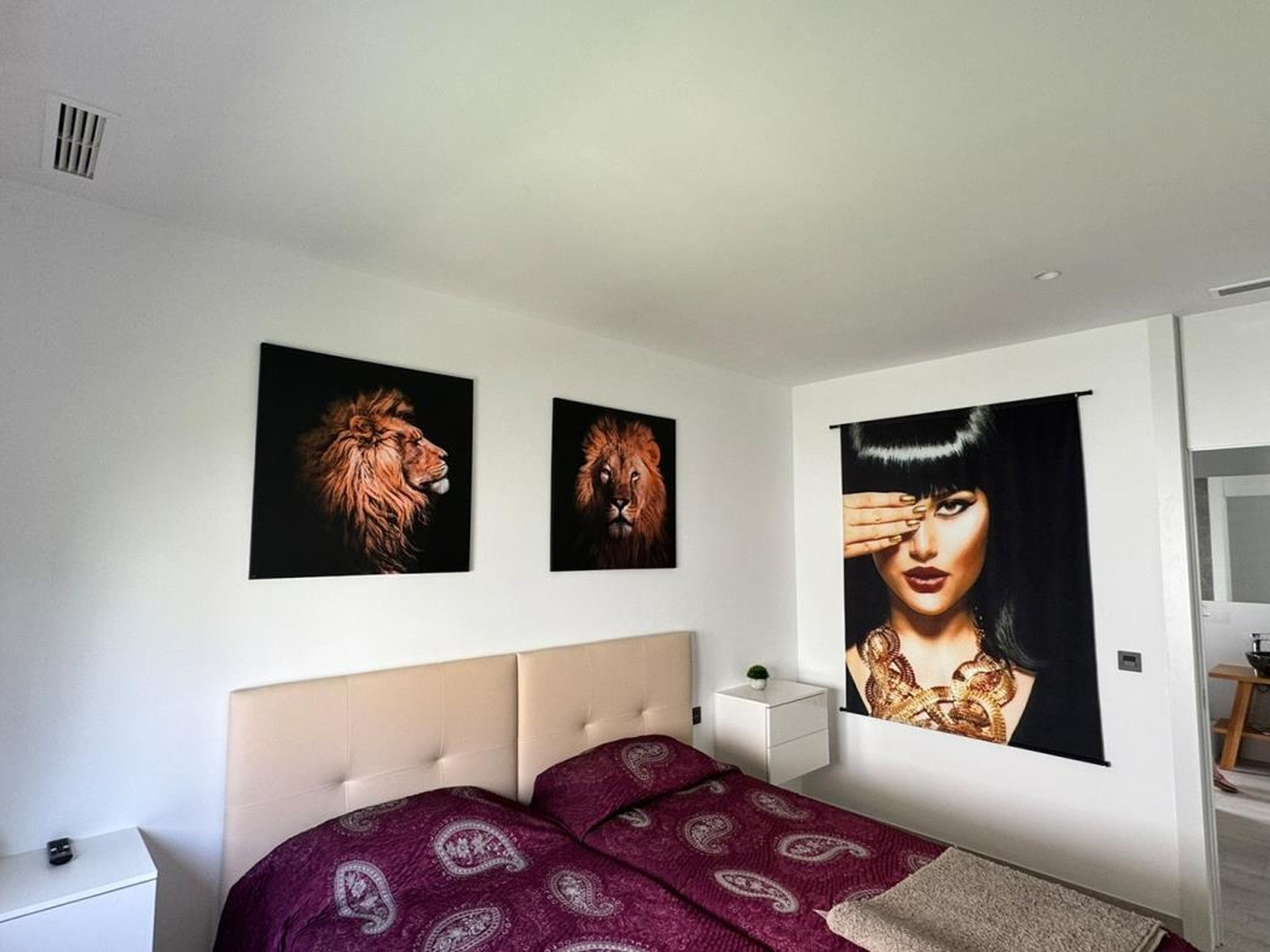 A bedroom with a bed, a nightstand, and two wall-mounted pictures.
