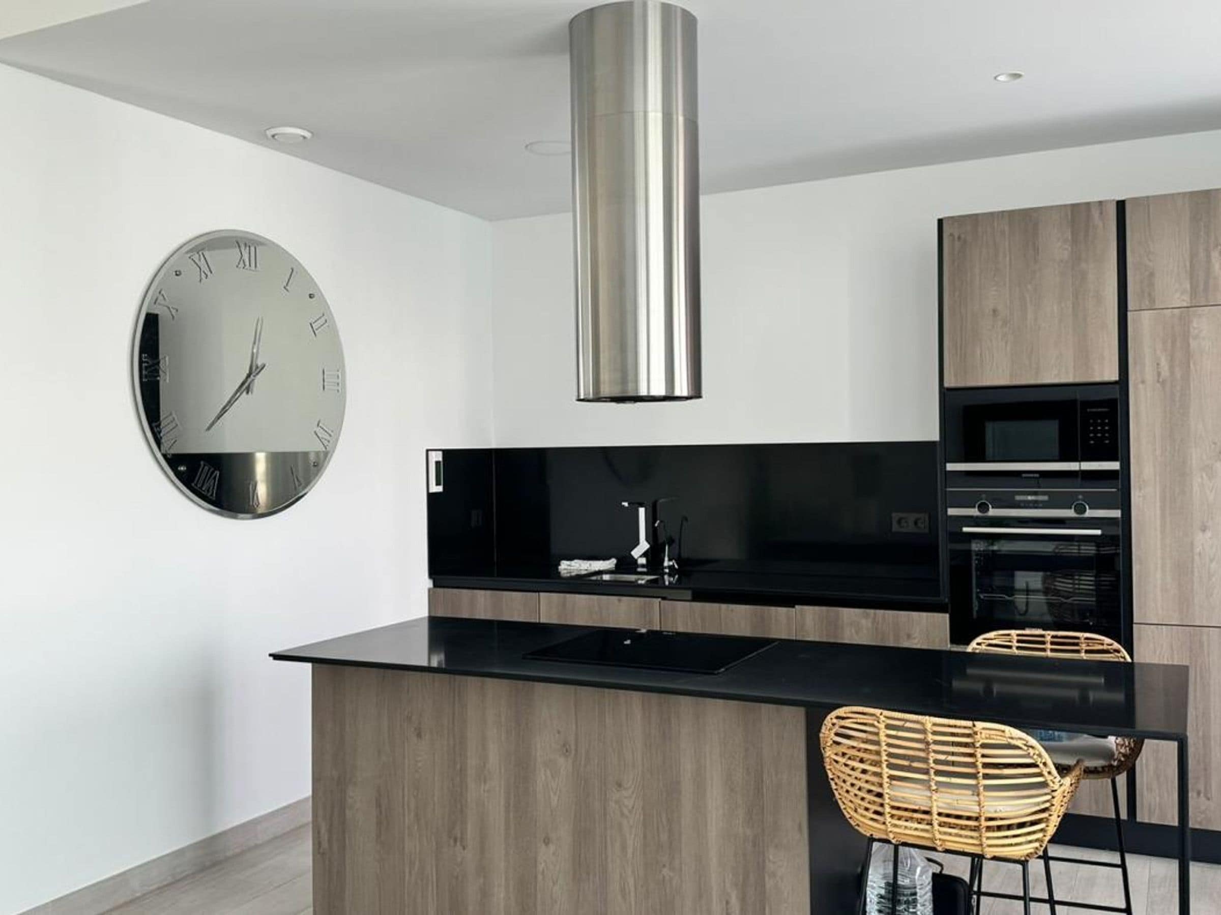 A modern kitchen with a central island, stainless steel appliances, and a wall-mounted clock.
