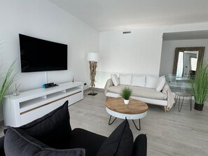 A modern living room with a flat-screen TV, a white sofa, a coffee table with a plant, and a glass dining table. - Villa with private pool - near beaches (Finestrat)