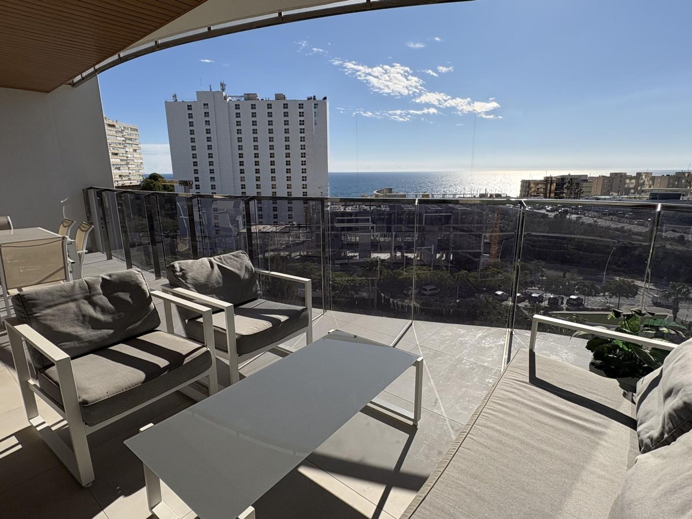 A balcony with a view of the sea and buildings, furnished with a sofa, chairs, and a table.