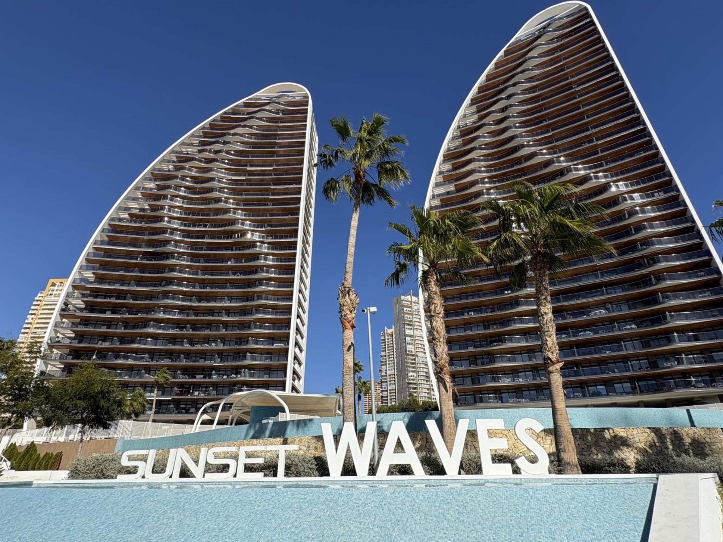 A modern hotel with a curved facade, multiple balconies, and a clear sky.