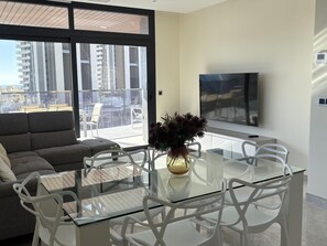 A modern living room with a glass table, white chairs, a grey sofa, and a large window overlooking a cityscape. - Spacious apartment, panoramic view - 6 guests (Benidorm)
