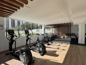 Een sportschool met trainingsapparatuur, grote ramen en een houten plafond.