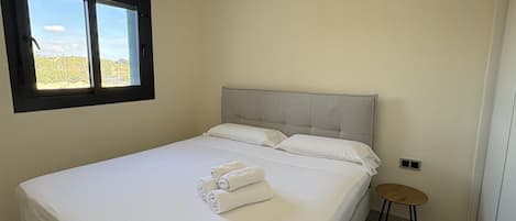 A single bed with a headboard, a small stool, and a window with a view of greenery.