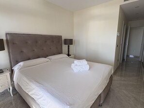 A hotel room with a large bed, a nightstand with a lamp, and a door leading to another room. - Spacious apartment, panoramic view - 6 guests (Benidorm)