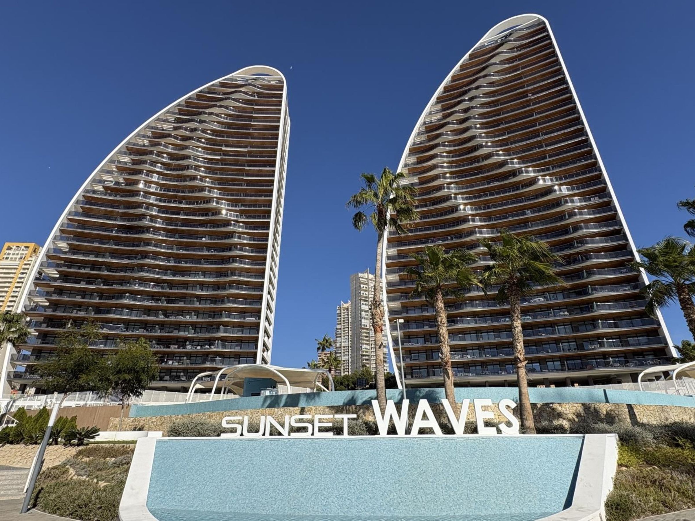 A modern high-rise building with a curved facade, labeled 'SUNSET WAVES.'