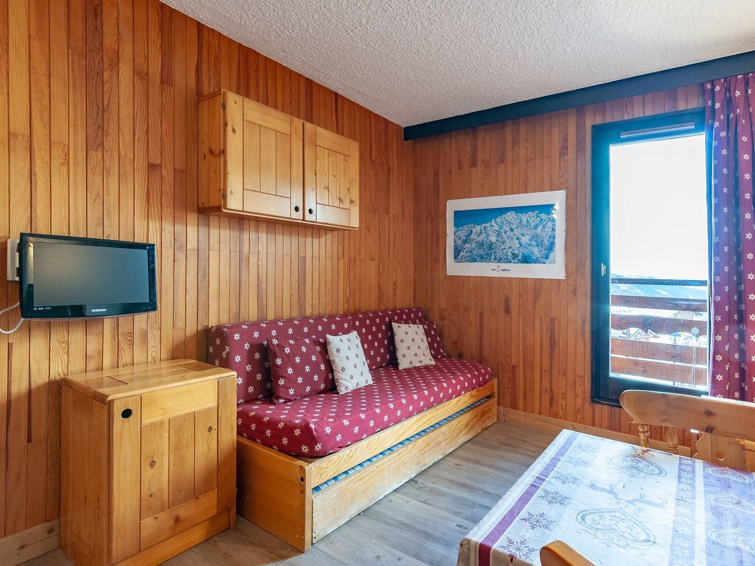 A wooden cabin interior with a sofa, a television mounted on the wall, and a window with a view.