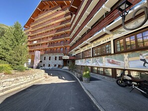 A multi-story hotel with a ski-themed mural on the facade, a stone wall entrance, and a motorcycle parked outside. - Charming apartment in Méribel (Méribel)