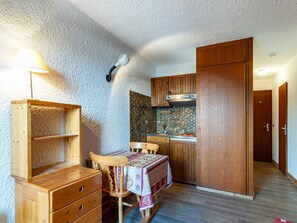 A compact kitchen with wooden cabinets, a built-in stove, and a dining area with a table and chairs. - Charming apartment in Méribel (Méribel)