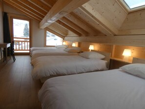 A room with four beds arranged in a row, wooden ceiling beams, and a view through a window. - Spacious chalet at the foot of the slopes - 12 guests (Arêches-Beaufort)