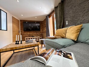 A modern living room with a sofa, a coffee table, and a flat-screen TV mounted on a brick wall. - New apartment with mountain view - 7 guests (Vars)