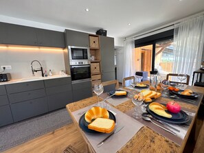 A modern kitchen with built-in appliances and a dining area with a wooden table set for a meal. - New apartment with mountain view - 7 guests (Vars)
