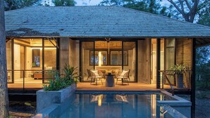 A modern house with a swimming pool, glass walls, and outdoor seating.