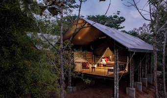 A tented accommodation with a wooden deck, a bed, and a small table.