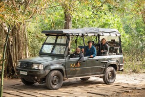 Un vehículo safari con la inscripción 'SAFARI LODGE' en la carrocería, estacionado en una zona boscosa.