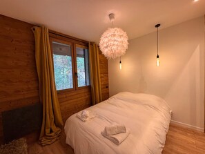 A bedroom with a large bed, wooden walls, a window with curtains, and a fluffy ceiling light fixture. - Spacious chalet with fireplace - 10 guests (Vars)