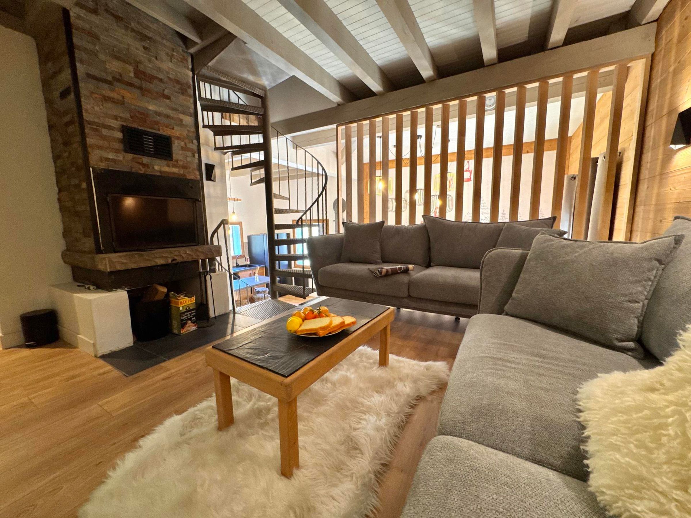 A cozy living room with a fireplace, a sofa, a coffee table with fruit, and a staircase.