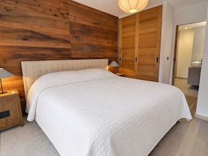 A bedroom with a large bed, wooden panel walls, and a nightstand with a lamp. - Spacious comfortable duplex - 12 guests (Méribel)