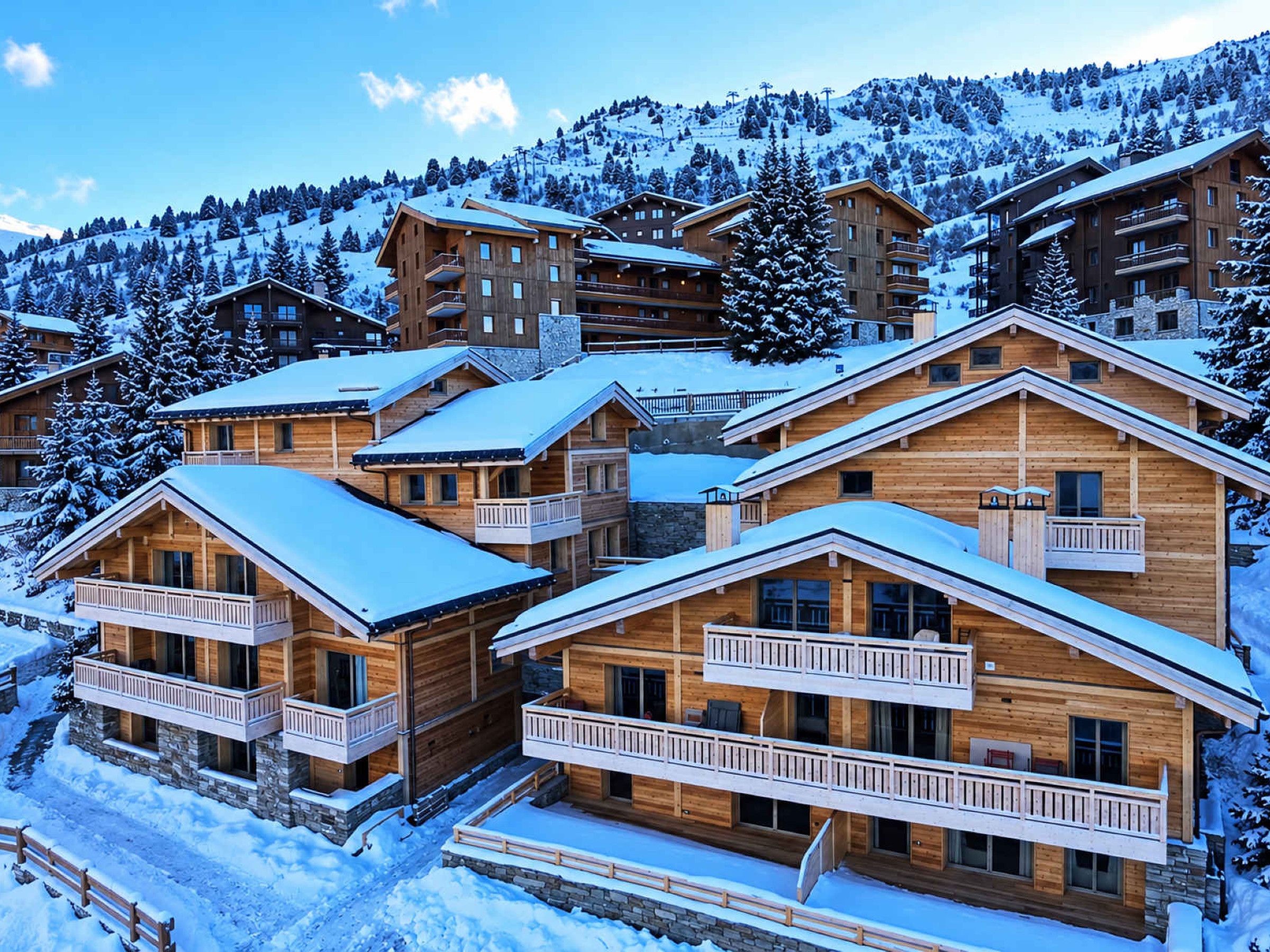 A cluster of wooden cabins with balconies, surrounded by snow-covered trees and a mountain backdrop.