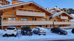 Una baita in legno con balconi, una seggiovia e un'area di parcheggio con auto.
