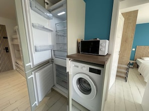 A compact laundry room with a washing machine and a microwave on a wooden shelf. - Quiet apartment with parking - 4 guests (La Grande-Motte)